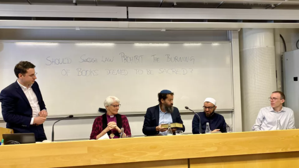Fem personer samtalar. Rabbinen håller i en helig skrift. Foto. 