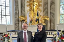 Martin Sunnqvist och Elsa Trolle Önnerfors i Göteborgs domkyrka med ett gyllene kors och blommor bakom sig. Foto.