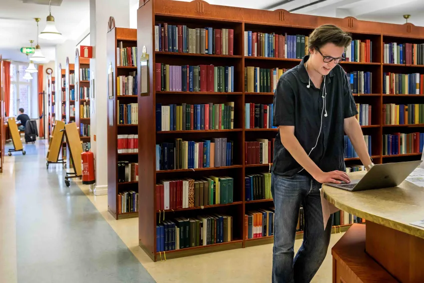 En student som står ensam vid sin bärbara dator i ett tomt bibliotek. Foto.